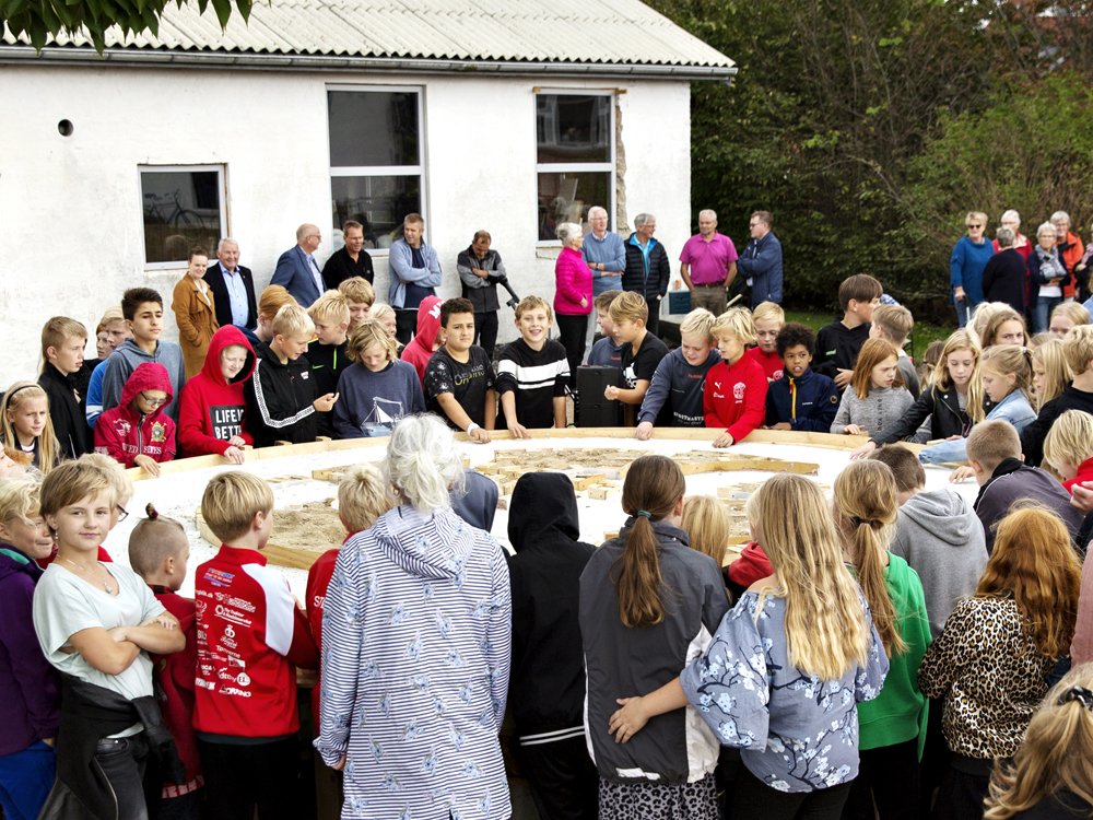 Børn og voksne står i en ring om et bord med ler