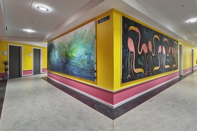 Gang med gule vægge, pink paneler og to malerier