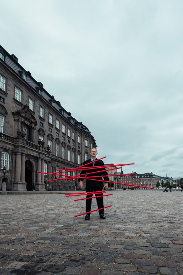 Mand står foran Christiansborg med røde stænger foran sig 
