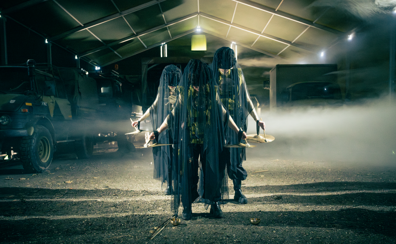 Tre personer i mørke kostumer, der dækker ansigterne, på scenen i en teaterforestilling